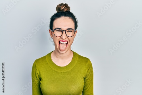 Young hispanic girl wearing casual clothes and glasses sticking tongue out happy with funny expression. emotion concept. © Krakenimages.com