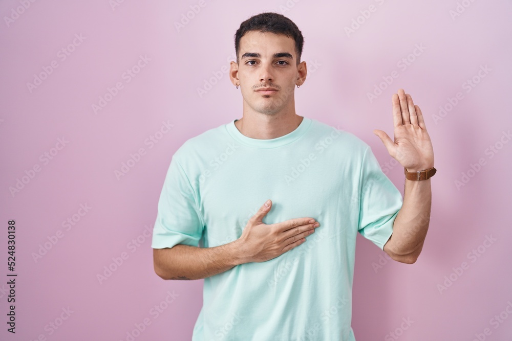 Handsome hispanic man standing over pink background swearing with hand on chest and open palm, making a loyalty promise oath Handsome hispanic man standing over pink background swearing with hand on chest and open palm, making a loyalty promise oath