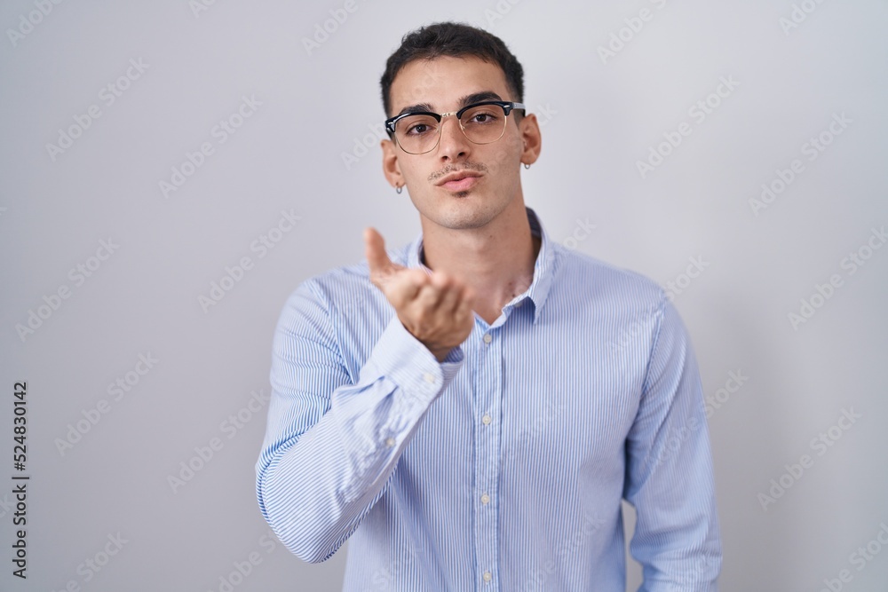 Handsome hispanic man wearing business clothes and glasses looking at the camera blowing a kiss with hand on air being lovely and sexy. love expression. Handsome hispanic man wearing business clothes and glasses looking at the camera blowing a kiss with hand on air being lovely and sexy. love expression.