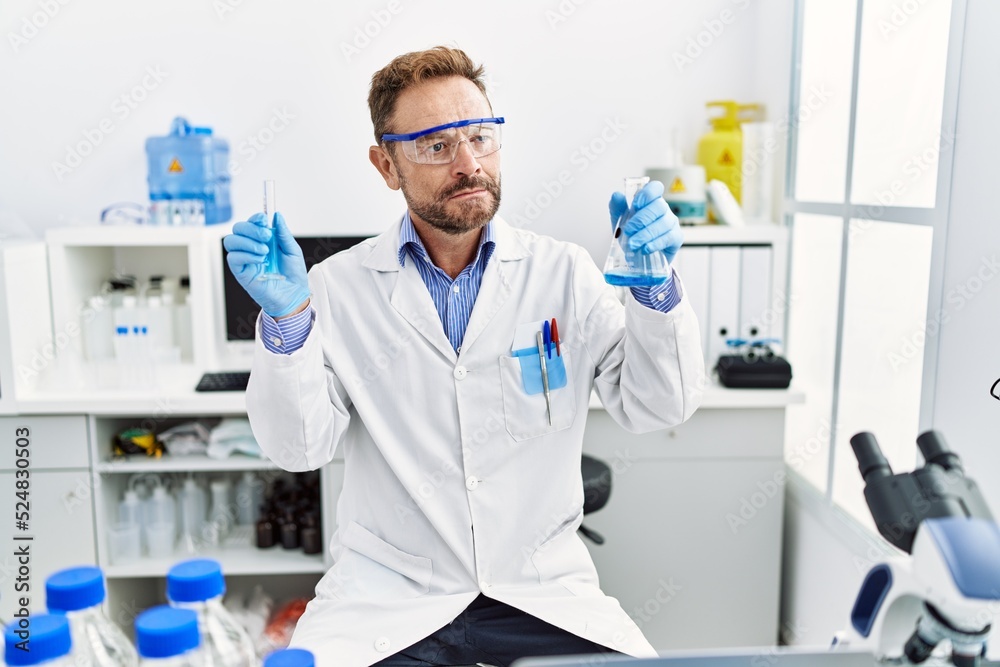Middle age man working at scientist laboratory holding chemical products smiling looking to the side and staring away thinking. Middle age man working at scientist laboratory holding chemical products smiling looking to the side and staring away thinking.