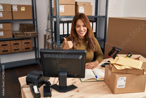 Hispanic woman working at small business ecommerce doing video call smiling happy and positive, thumb up doing excellent and approval sign