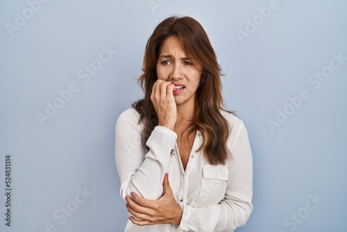 Hispanic woman standing over isolated background looking stressed and nervous with hands on mouth biting nails. anxiety problem.
