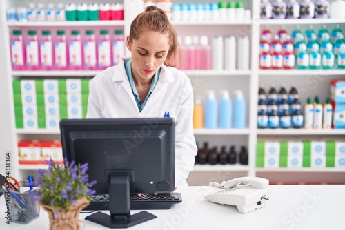 Young beautiful hispanic woman pharmacist using computer with serious expression at pharmacy