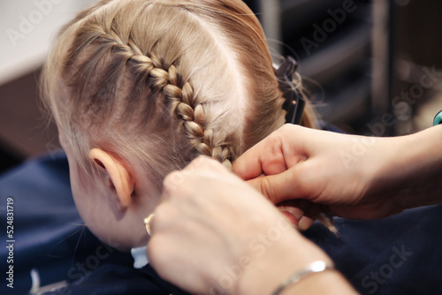 Foto Hair salon, hairdresser makes hairdo braids for young baby in barber shop
