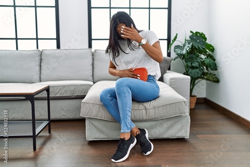 Young latin woman using hot water bag for menstrual pain at home