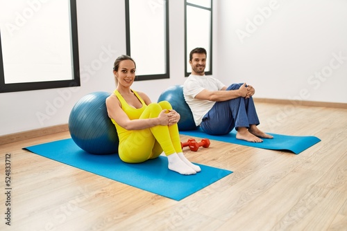 Young hispanic couple training using fit ball at sport center.