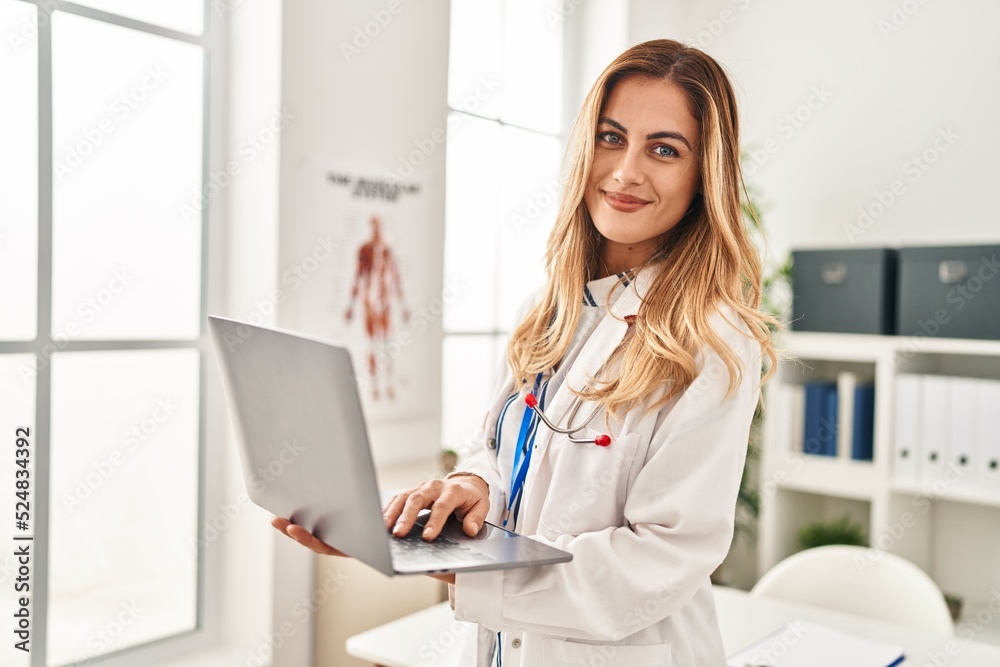Young blonde woman wearing doctor uniform using laptop at clinic Young blonde woman wearing doctor uniform using laptop at clinic
