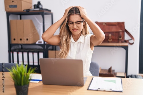 Young blonde woman working at the office wearing glasses suffering from headache desperate and stressed because pain and migraine. hands on head.