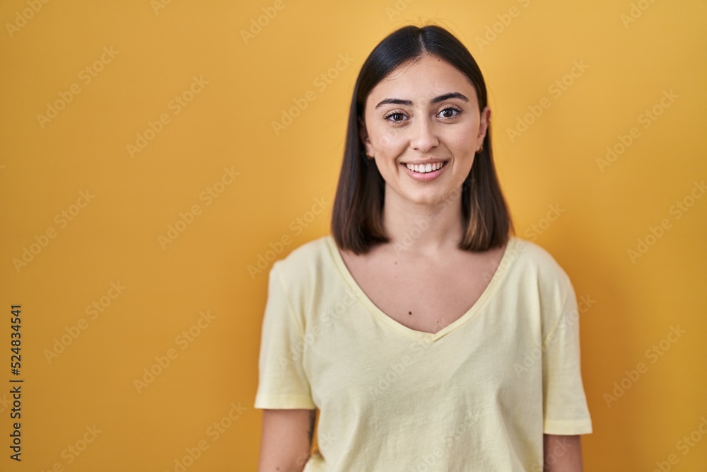 Hispanic girl wearing casual t shirt over yellow background with a happy and cool smile on face. lucky person. Hispanic girl wearing casual t shirt over yellow background with a happy and cool smile on face. lucky person.
