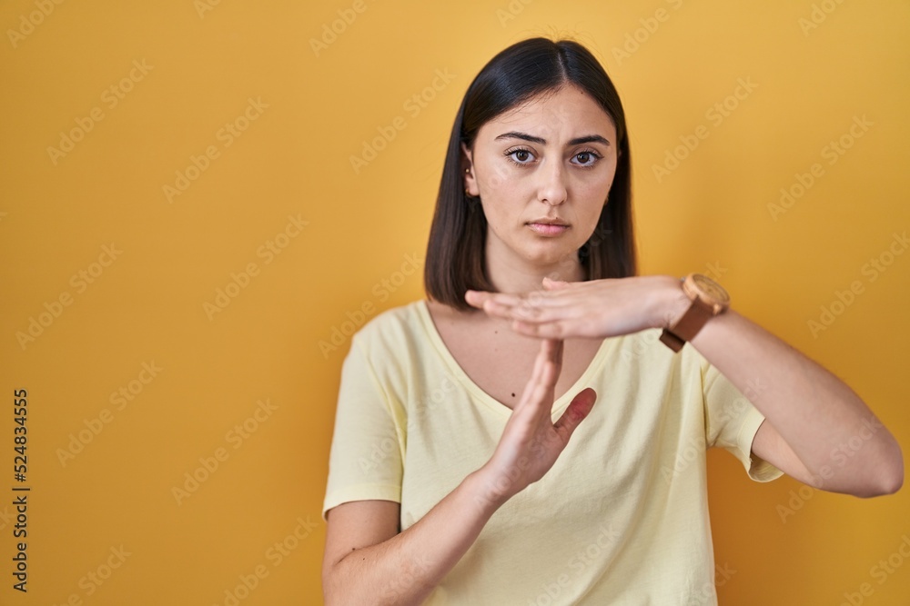 Hispanic girl wearing casual t shirt over yellow background doing time out gesture with hands, frustrated and serious face Hispanic girl wearing casual t shirt over yellow background doing time out gesture with hands, frustrated and serious face