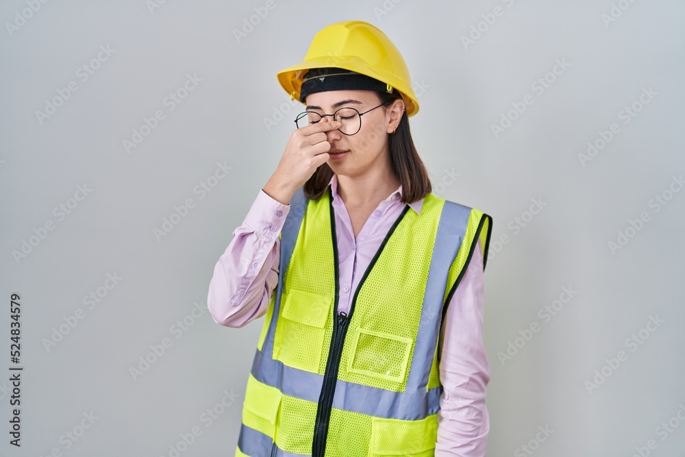Hispanic girl wearing builder uniform and hardhat tired rubbing nose and eyes feeling fatigue and headache. stress and frustration concept. Hispanic girl wearing builder uniform and hardhat tired rubbing nose and eyes feeling fatigue and headache. stress and frustration concept.