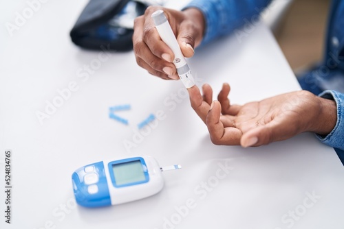 Young latin man measuring glucose sitting on table at home