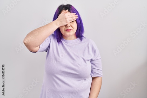 Plus size woman wit purple hair standing over isolated background smiling and laughing with hand on face covering eyes for surprise. blind concept. © Krakenimages.com