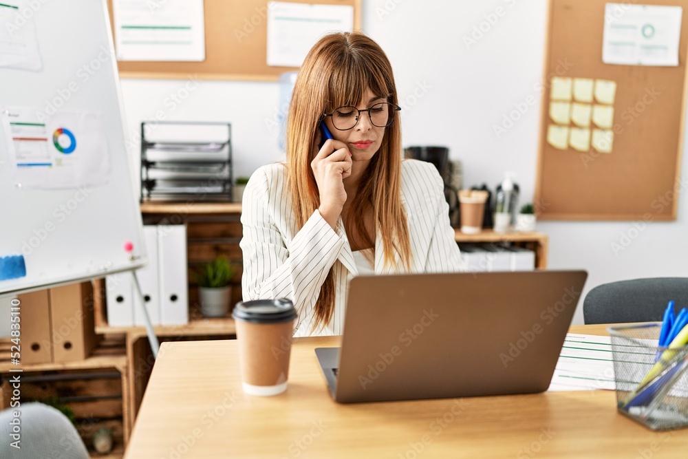 Obraz premium Young hispanic businesswoman working talking on the smartphone and using laptop at the office.