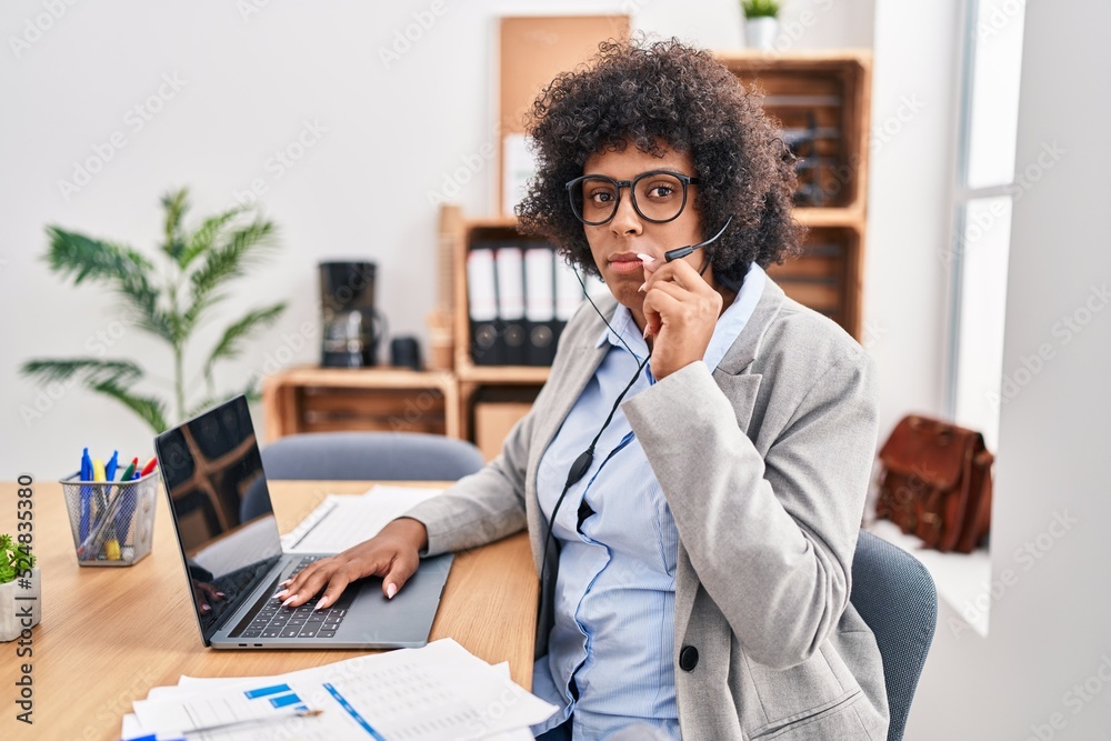 Black woman with curly hair wearing call center agent headset at the office mouth and lips shut as zip with fingers. secret and silent, taboo talking Black woman with curly hair wearing call center agent headset at the office mouth and lips shut as zip with fingers. secret and silent, taboo talking