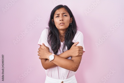 Young hispanic woman standing over pink background shaking and freezing for winter cold with sad and shock expression on face