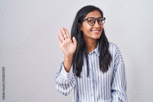 Young hispanic woman wearing glasses waiving saying hello happy and smiling, friendly welcome gesture
