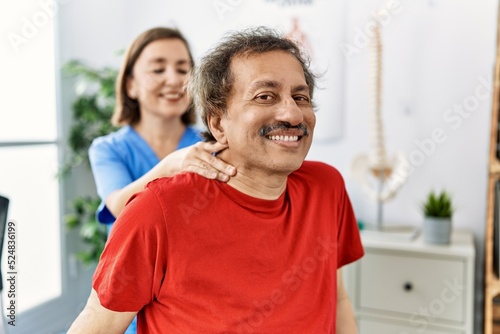 Middle age man and woman wearing physiotherapy uniform having rehab session massaging neck at physiotherapy clinic