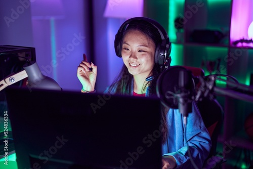 Young asian woman playing video games smiling happy pointing with hand and finger to the side