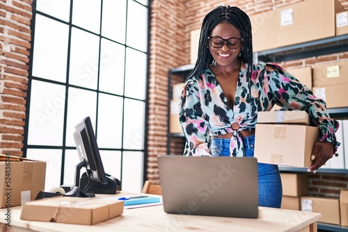 African american woman ecommerce business worker using laptop holding packages at office