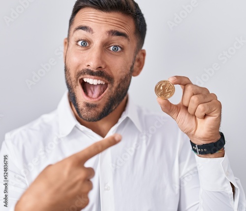 Handsome hispanic man holding litecoin cryptocurrency coin smiling happy pointing with hand and finger photo