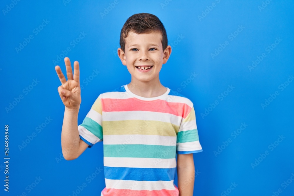 Young caucasian kid standing over blue background showing and pointing up with fingers number three while smiling confident and happy. Young caucasian kid standing over blue background showing and pointing up with fingers number three while smiling confident and happy.