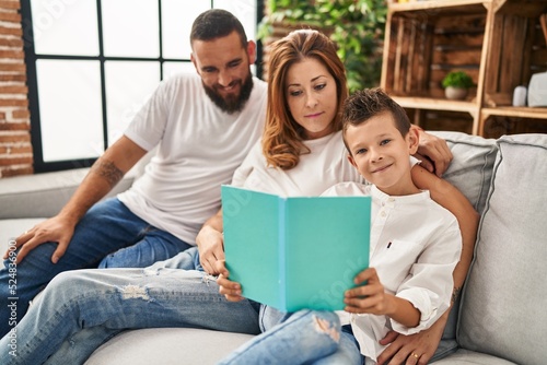Family reading book sitting on sofa at home
