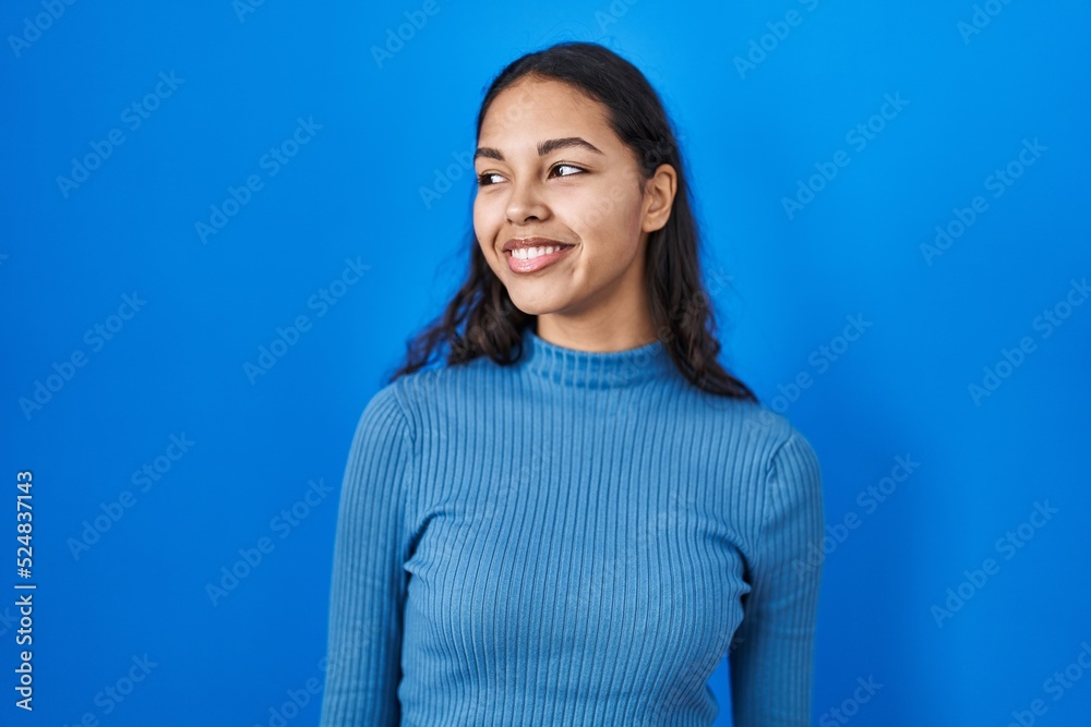 Obraz premium Young brazilian woman standing over blue isolated background smiling looking to the side and staring away thinking.