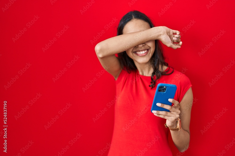 Young brazilian woman using smartphone over red background smiling cheerful playing peek a boo with hands showing face. surprised and exited Young brazilian woman using smartphone over red background smiling cheerful playing peek a boo with hands showing face. surprised and exited