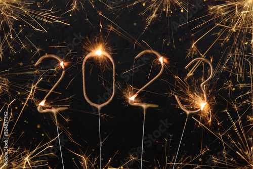 Happy New Year 2023 Silvester party card. Digits of year 2023 made by golden burning sparklers with sparks and glitter lights bokeh.