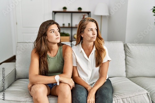 Mother and daughter together sitting on the sofa at home looking to side, relax profile pose with natural face and confident smile.
