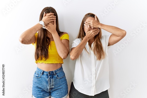 Mother and daughter together standing together over isolated background covering eyes and mouth with hands, surprised and shocked. hiding emotion