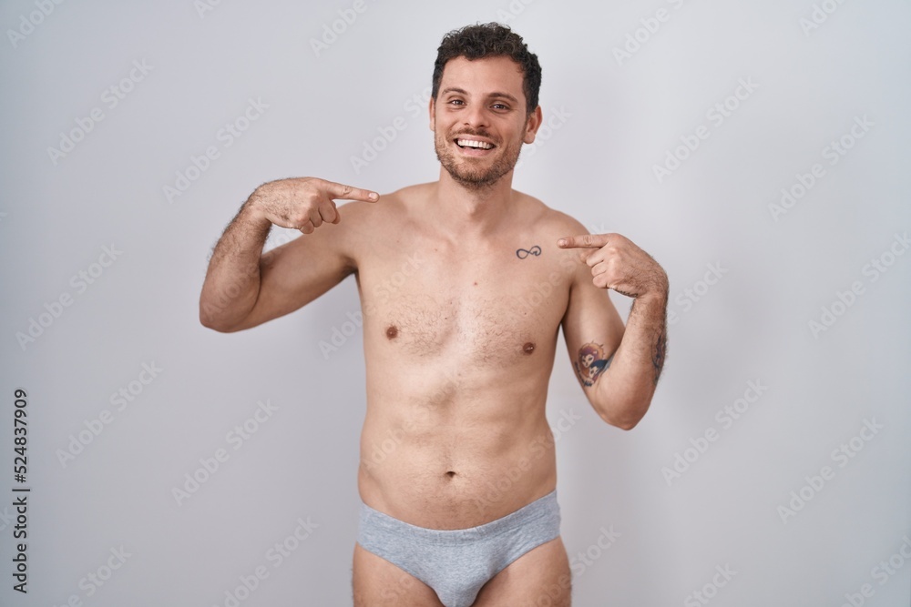 Young hispanic man standing shirtless wearing underware looking confident with smile on face, pointing oneself with fingers proud and happy.