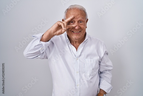Senior man with grey hair standing over isolated background doing peace symbol with fingers over face, smiling cheerful showing victory