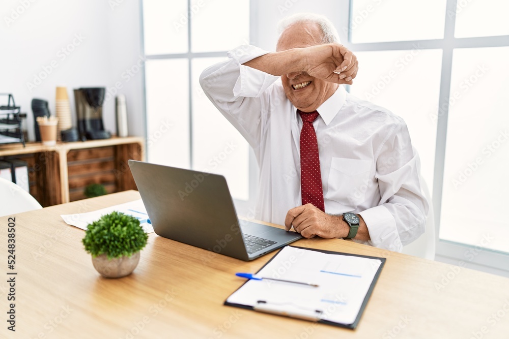Senior man working at the office using computer laptop covering eyes with arm smiling cheerful and funny. blind concept. Senior man working at the office using computer laptop covering eyes with arm smiling cheerful and funny. blind concept.