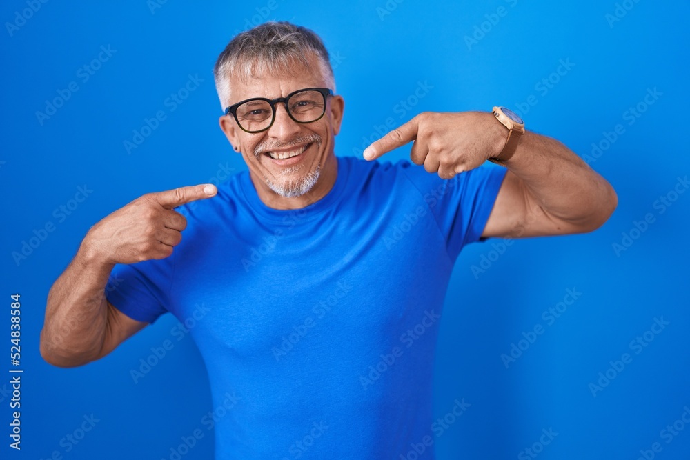 Naklejka premium Hispanic man with grey hair standing over blue background smiling cheerful showing and pointing with fingers teeth and mouth. dental health concept.