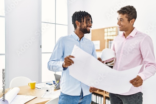 Two men architect workers smiling confident holding blueprint standing at architecture studio