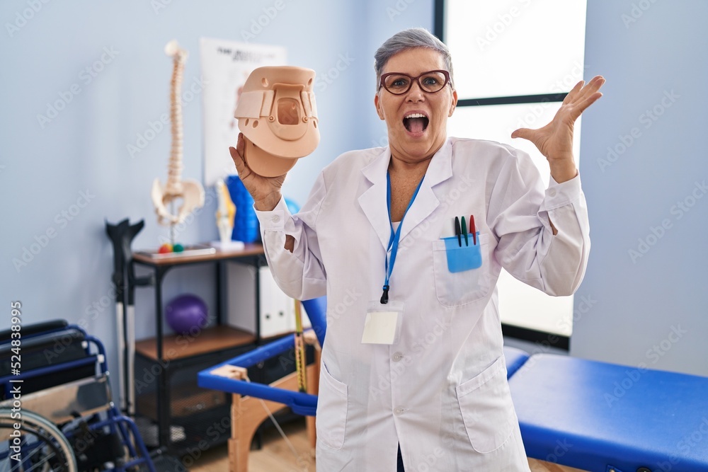 Middle age woman holding cervical neck collar celebrating victory with happy smile and winner expression with raised hands