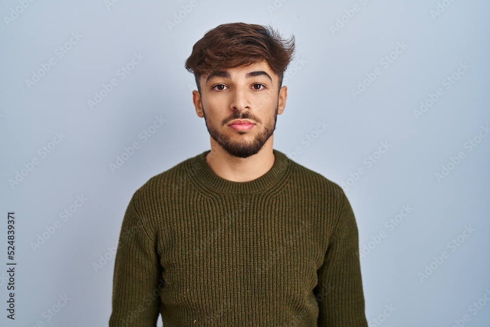 Arab man with beard standing over blue background relaxed with serious expression on face. simple and natural looking at the camera. Arab man with beard standing over blue background relaxed with serious expression on face. simple and natural looking at the camera.