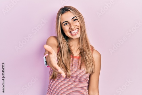 Beautiful hispanic woman wearing casual summer t shirt smiling cheerful offering palm hand giving assistance and acceptance.