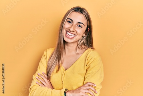 Beautiful hispanic woman wearing casual yellow sweater happy face smiling with crossed arms looking at the camera. positive person. © Krakenimages.com
