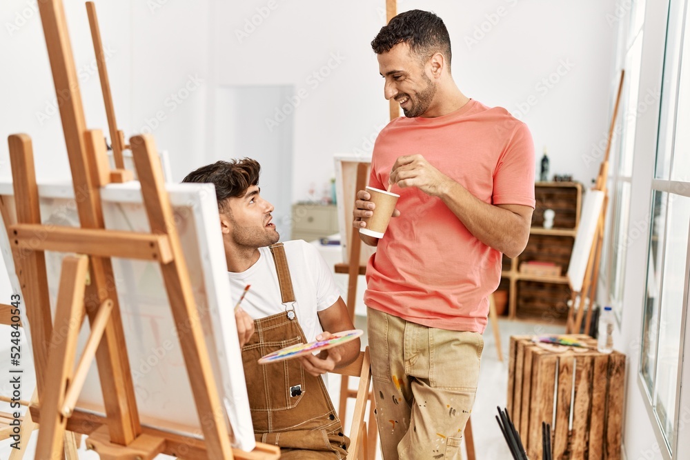 Two hispanic men couple smiling confident drinking coffee and drawing at art studio