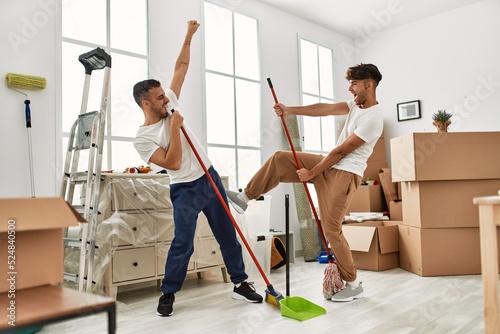 Two hispanic men couple cleaning and dancing at new home