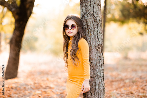 Cute stylish child girl 4-5 year old wear yellow knitted dress and sun glasses posing in park outdoor. Fall season. Childhood. © morrowlight
