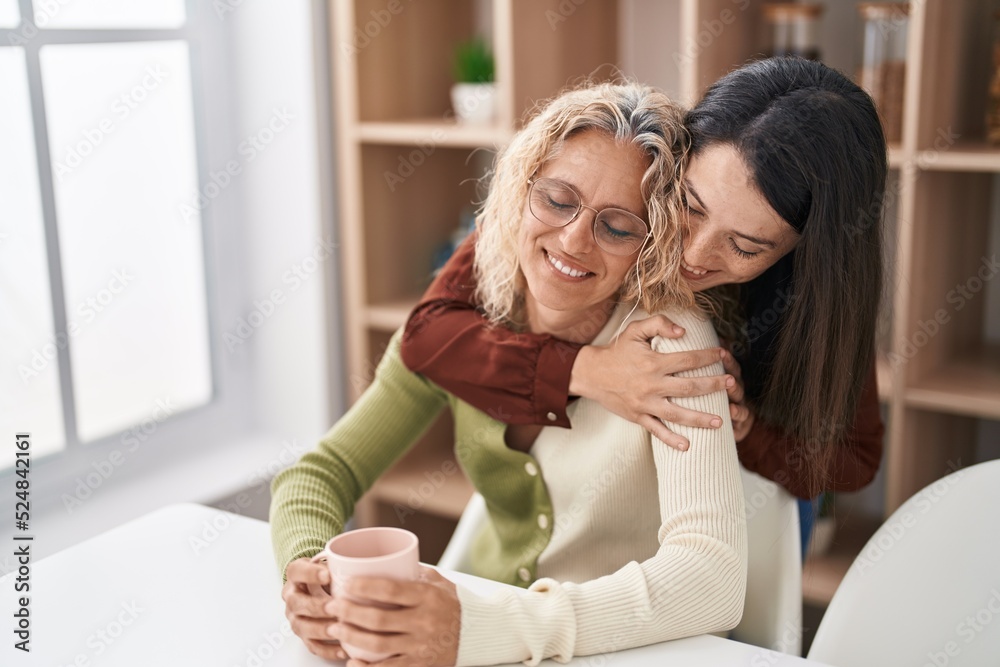 Two women mother and daughter hugging each other drinking coffee at home Two women mother and daughter hugging each other drinking coffee at home