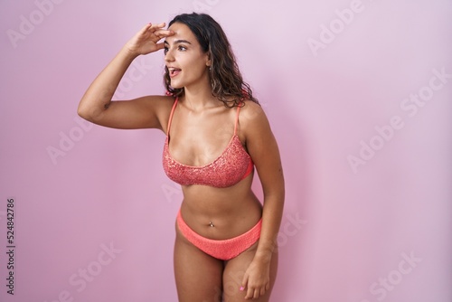 Young hispanic woman wearing lingerie over pink background very happy and smiling looking far away with hand over head. searching concept. © Krakenimages.com