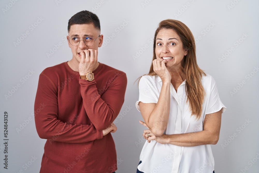 Mother and son standing together over isolated background looking stressed and nervous with hands on mouth biting nails. anxiety problem. Mother and son standing together over isolated background looking stressed and nervous with hands on mouth biting nails. anxiety problem.