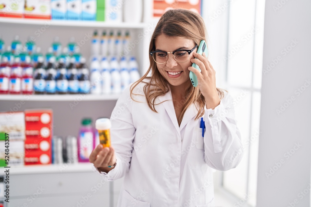 Young woman pharmacist holding pills bottle talking on smartphone at pharmacy Young woman pharmacist holding pills bottle talking on smartphone at pharmacy