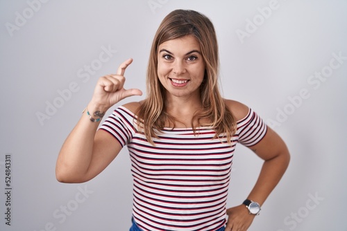Young hispanic woman standing over isolated background smiling and confident gesturing with hand doing small size sign with fingers looking and the camera. measure concept. © Krakenimages.com