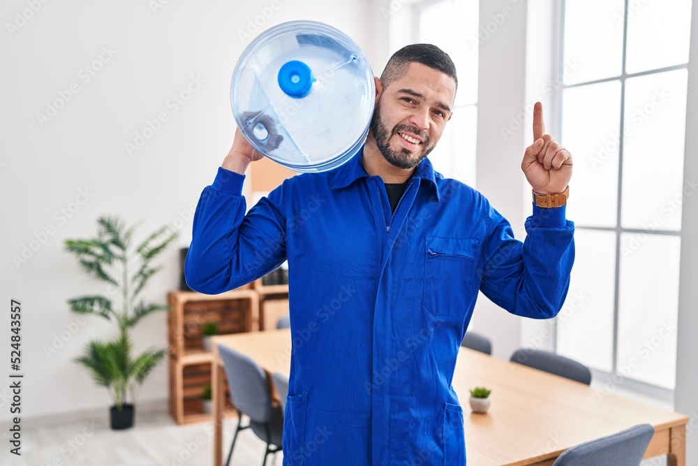Hispanic service man holding a gallon bottle of water for delivery surprised with an idea or question pointing finger with happy face, number one Hispanic service man holding a gallon bottle of water for delivery surprised with an idea or question pointing finger with happy face, number one